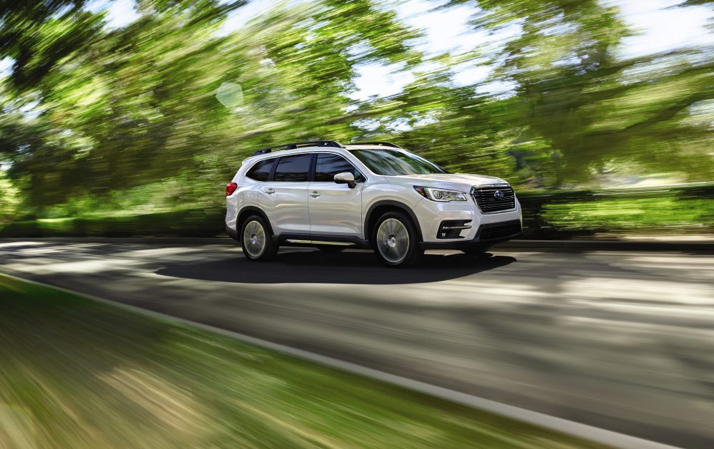 A white 2021 Subaru Ascent speeding down a scenic road with motion-blur