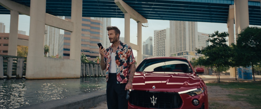 David Beckham holding his phone in front of a red Maserati Levante Trofeo