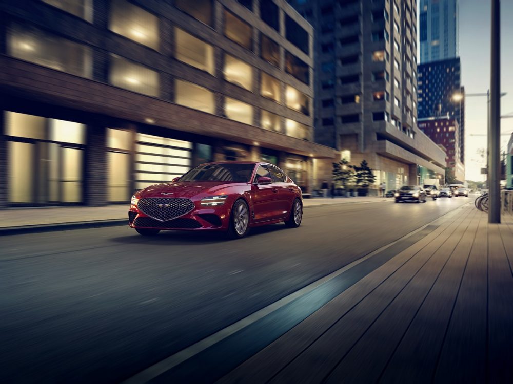 Front side view of 2022 Genesis G70 driving down city street at night