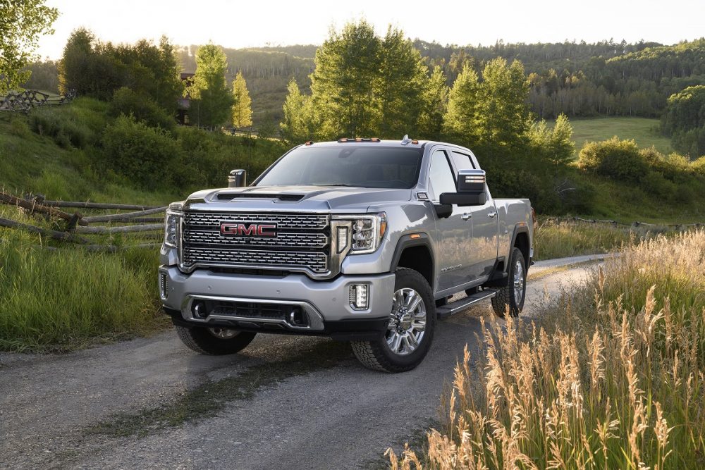 2021 GMC Sierra driving on a gravel road with trees and hills in the background