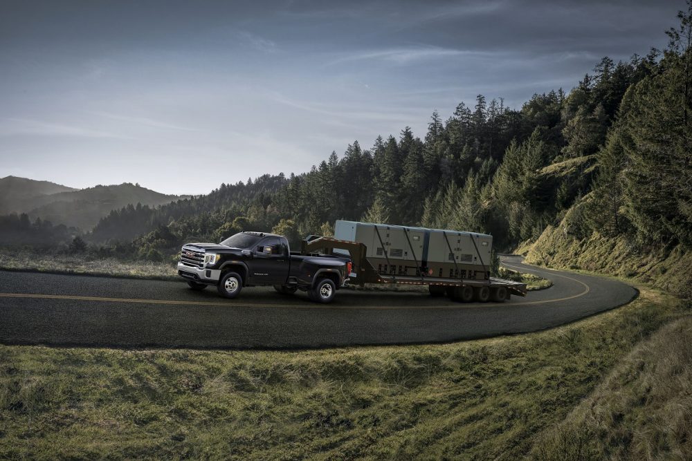 Side view of 2021 GMC Sierra 3500HD pulling heavy trailer up hilly road