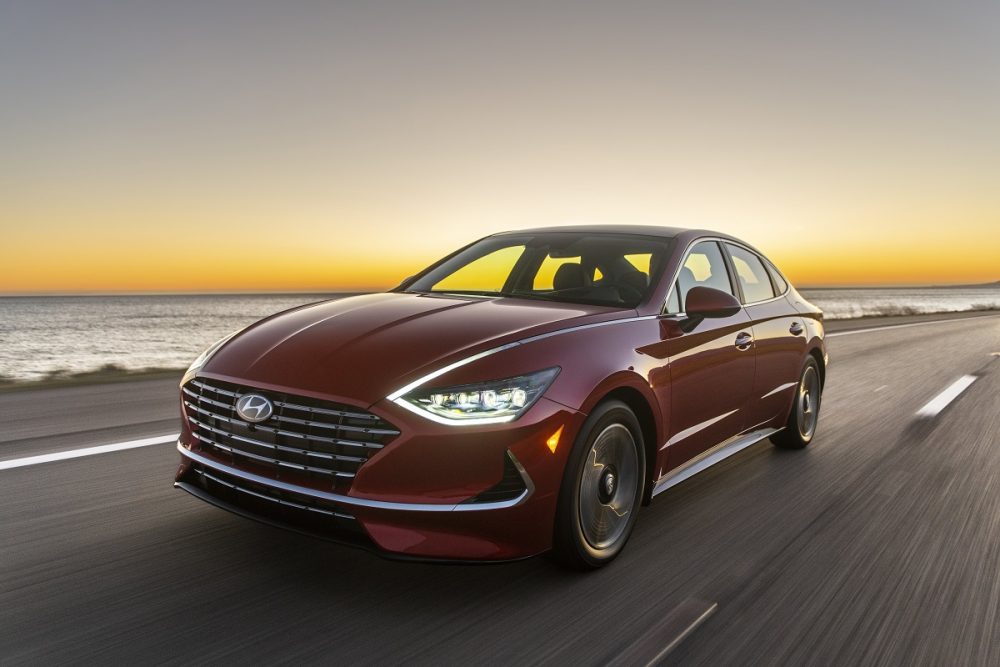 Front side view of 2021 Sonata Hybrid driving down road with headlights on