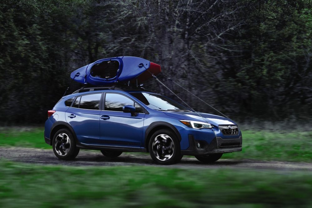 A blue 2021 Subaru Crosstrek with a blue kayak atop drives across an off-road trail