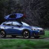 A blue 2021 Subaru Crosstrek with a blue kayak atop drives across an off-road trail