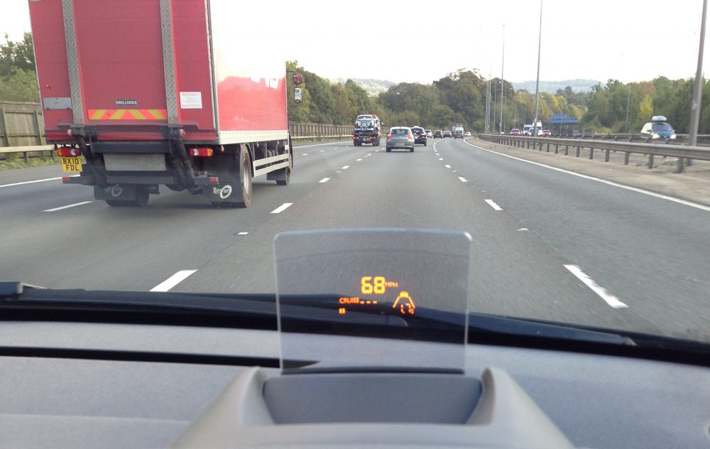 A head-up display showing vehicle speed on a car driving on a British motorway.