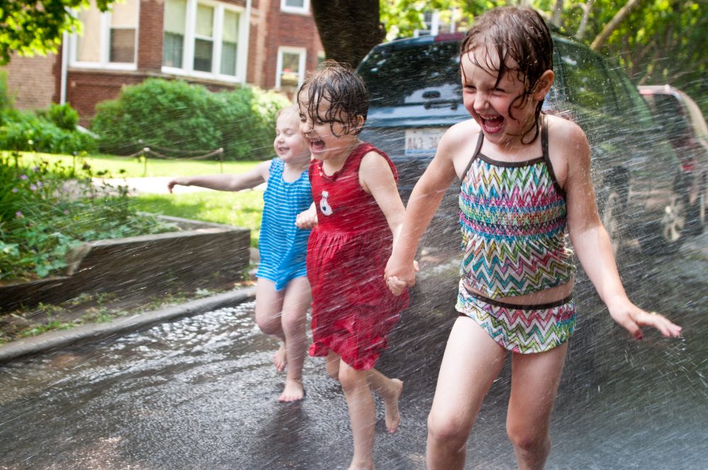 Children near a parked car playing in a fire hydrant on a hot day