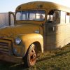 A woman gives a thumbs up from the front seat of a rusted 1955 school bus parked in grass