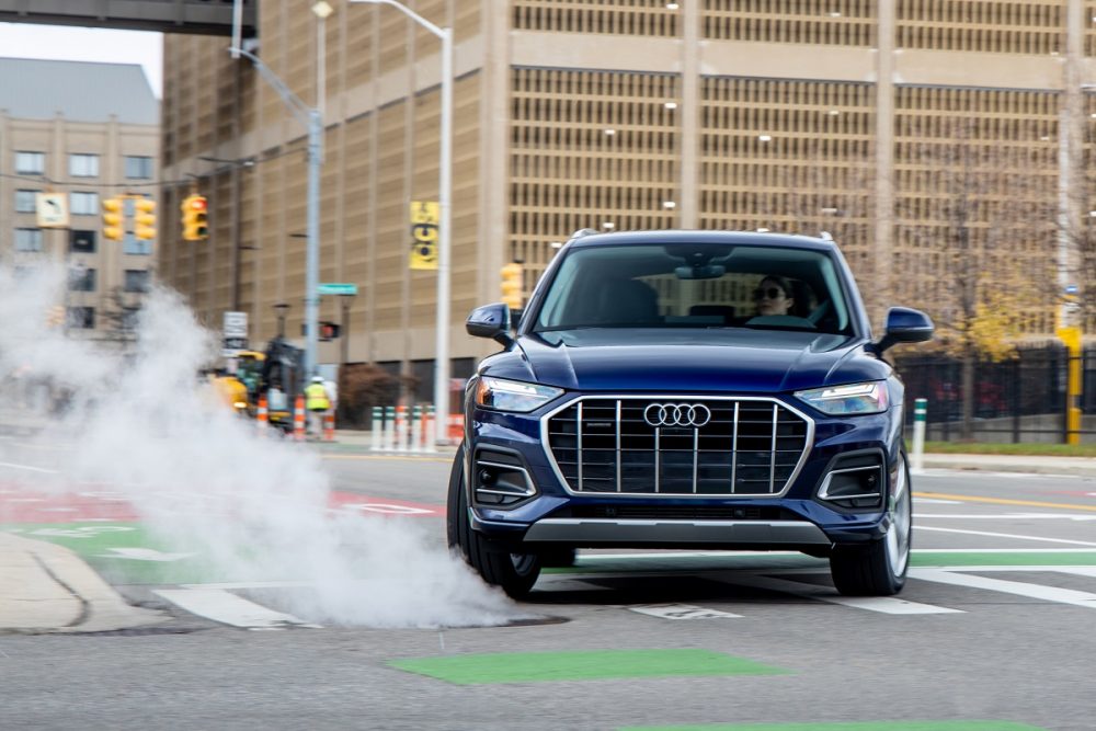 A dark blue 2021 Audi Q5 drifts on city streets while clouds of smoke come from the tires