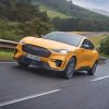 A Cyber Orange 2021 Ford Mustang Mach-E GT races along a country road in the United Kingdom