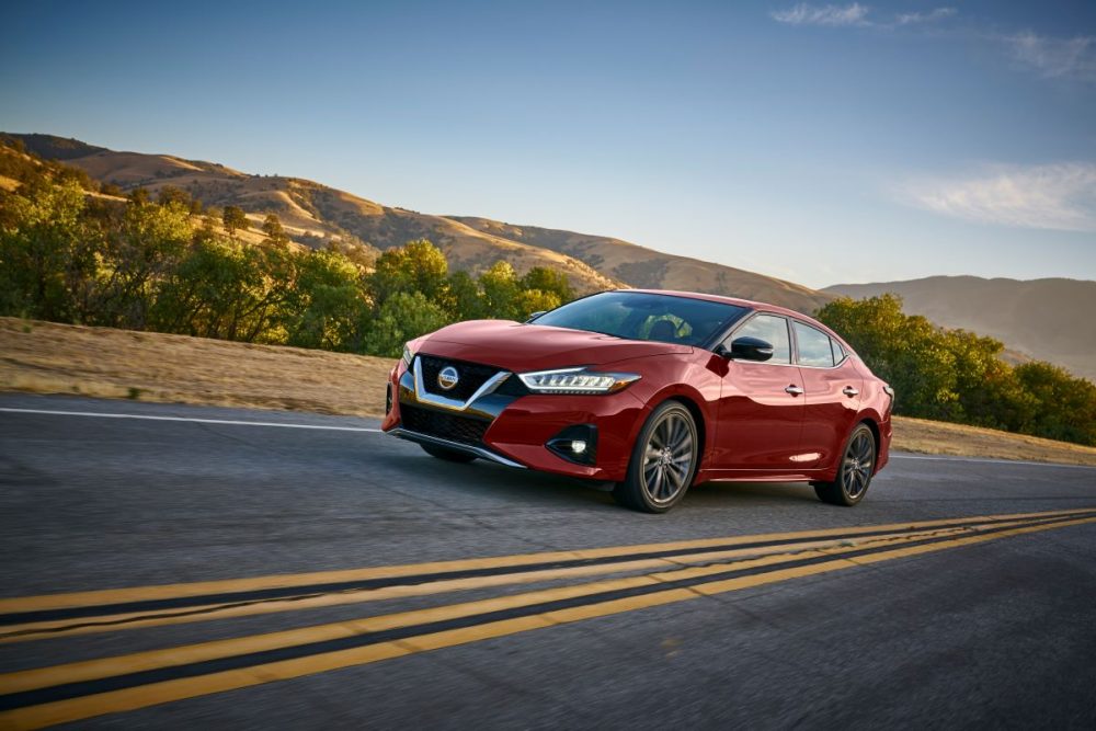 Red 2021 Nissan Maxima driving on highway with mountains and trees in the distance