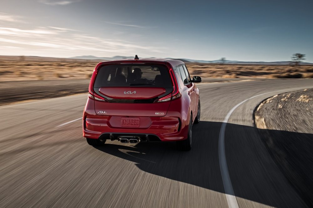 Exterior rear photo of a red 2022 Kia Soul driving around a curve on a deserted road