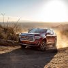 Front side view of GMC Acadia Denali driving up dusty desert road