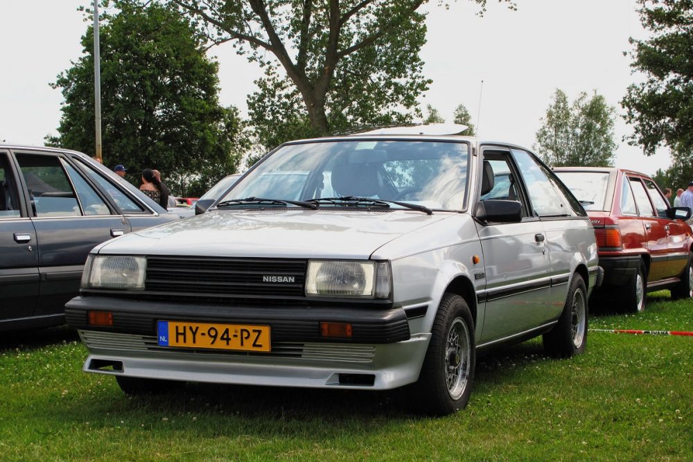 A light gray/silver 1982 Nissan Sunny (also called the Sentra) parked on grass at an auto show in Japan