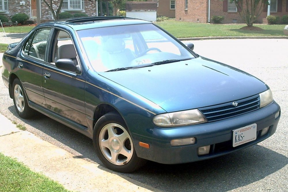 A blueish green 1995 Nissan Altima parked in a cul-de-sac within a neighborhood