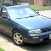 A blueish green 1995 Nissan Altima parked in a cul-de-sac within a neighborhood