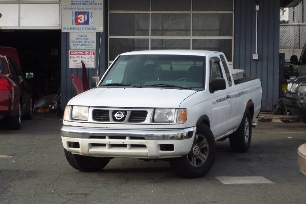 A white 2000 Nissan Frontier parked in front of an auto body shop