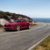 Front side view of red 2021 Chevrolet Camaro driving around the curve of a mountainous road with a body of water in the background