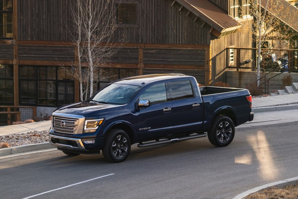 A dark blue 2021 Nissan TITAN is parked at sunset on a street in front of a large cabin in a mountain town