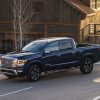 A dark blue 2021 Nissan TITAN is parked at sunset on a street in front of a large cabin in a mountain town