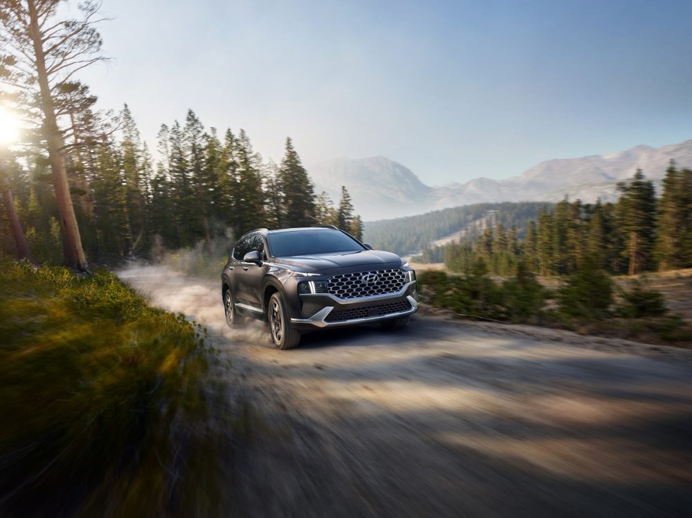 Front side view of gray 2021 Hyundai Santa Fe Hybrid driving on dusty mountain road