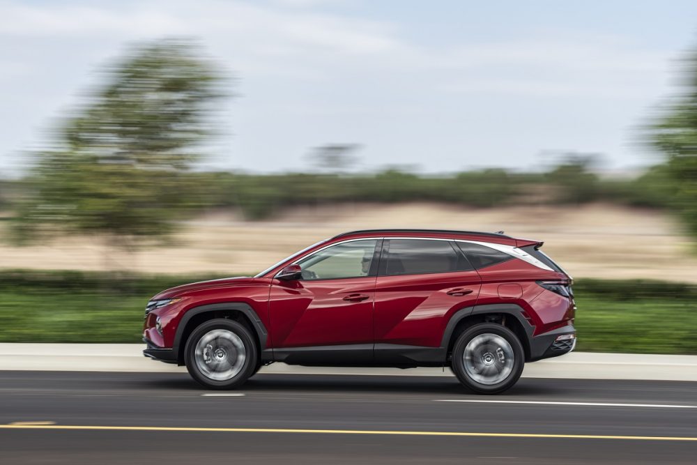 Profile view of red 2022 Hyundai Tucson driving down road