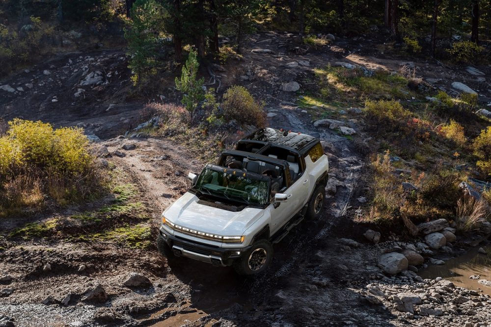 Aerial view of a white 2024 GMC Hummer EV SUV traversing across rocks and water