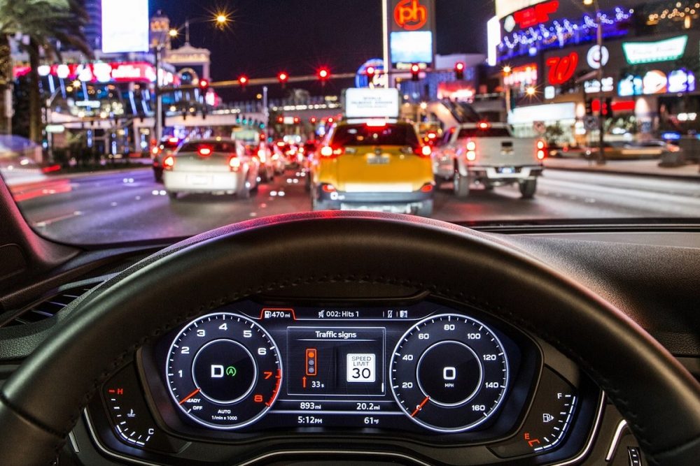 Close up of Audi steering wheel and vehicle information display with nighttime city in front of the vehicle