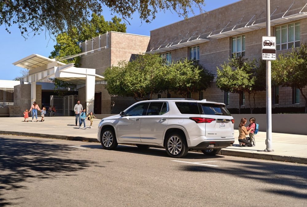 A Chevrolet Traverse is parked in front of a school building with children and parents nearby