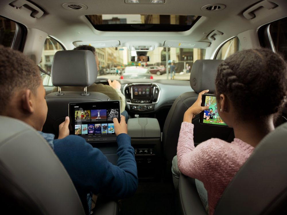 Two young children hold tablets and watch videos in the second row of a GM vehicle