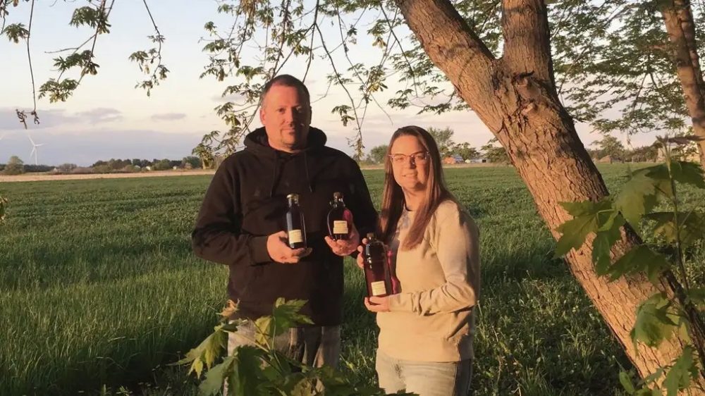 Jarrod Fortin standing with maple syrup by a maple tree at his property in South Woodslee