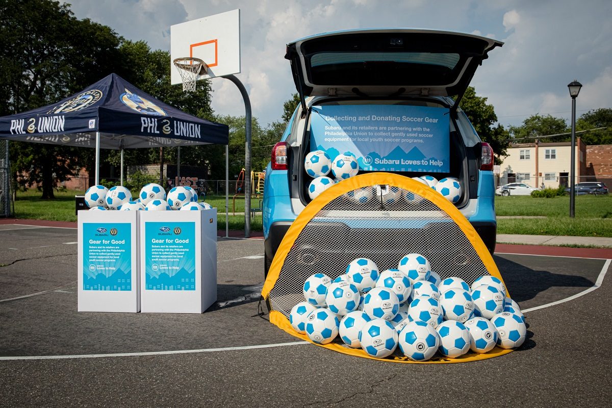 A Subaru vehicle parked with a pile of soccer balls and a net in front of it