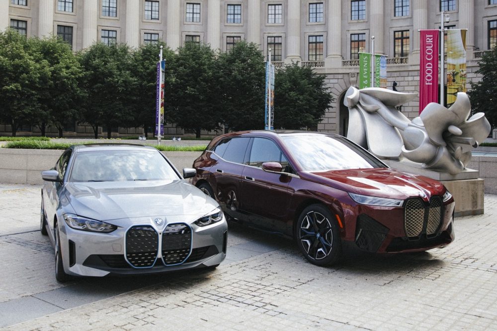 Two 2022 BMW iX models (silver on the left and maroon on the right) are parked in front of a historic building in the U.S.