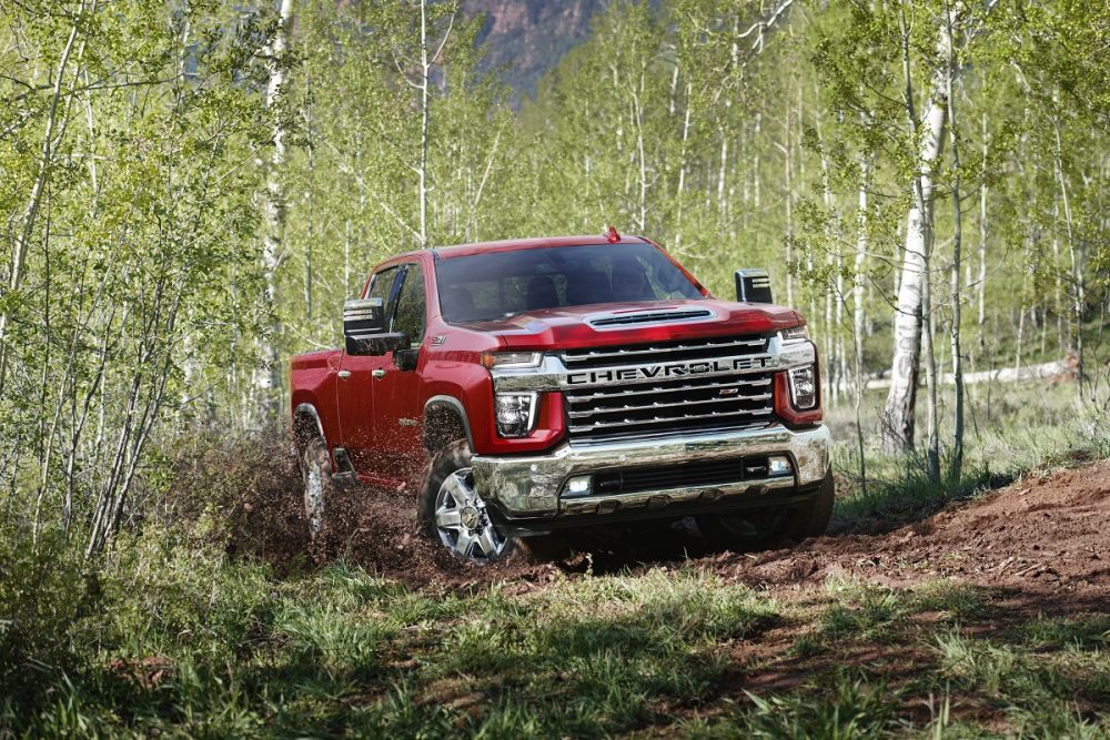 A red 2022 Chevrolet Silverado 2500HD drives through a forest area