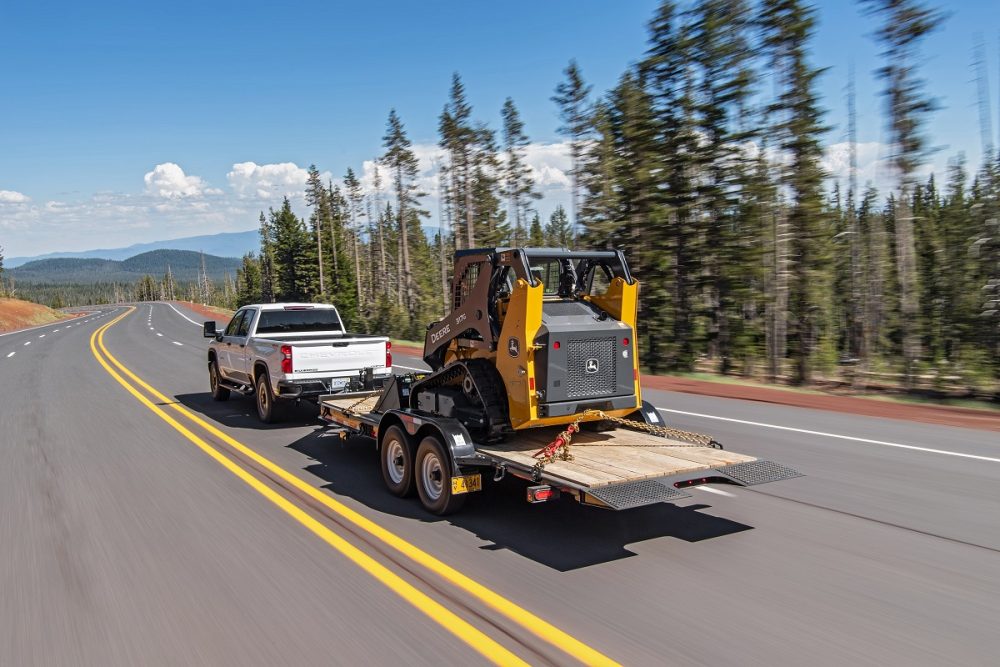 A white 2022 Chevrolet Silverado 2500HD tows work equipment on a highway