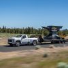 A white 2022 Chevrolet Silverado 3500HD tows a gigantic Chevrolet anvil