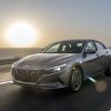 Front side view of Hyundai Elantra Hybrid driving down road with sea and setting sun in background