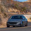 Front side view of 2022 Hyundai Elantra driving around curve with grassy hills in background