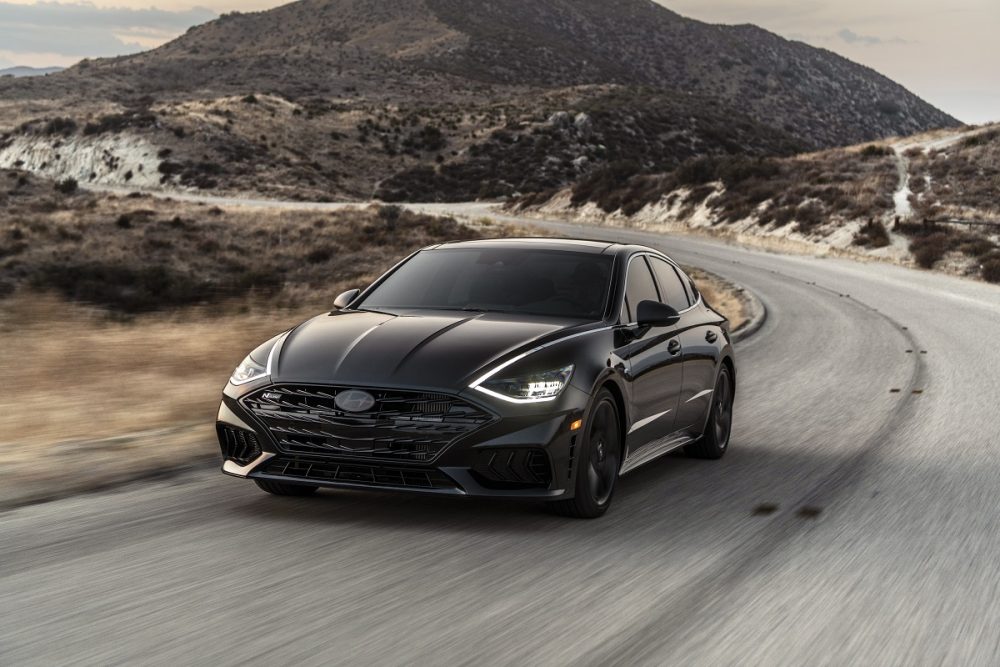 Front side view of 2022 Hyundai Sonata N Line Night Edition driving around curve with large hill in background