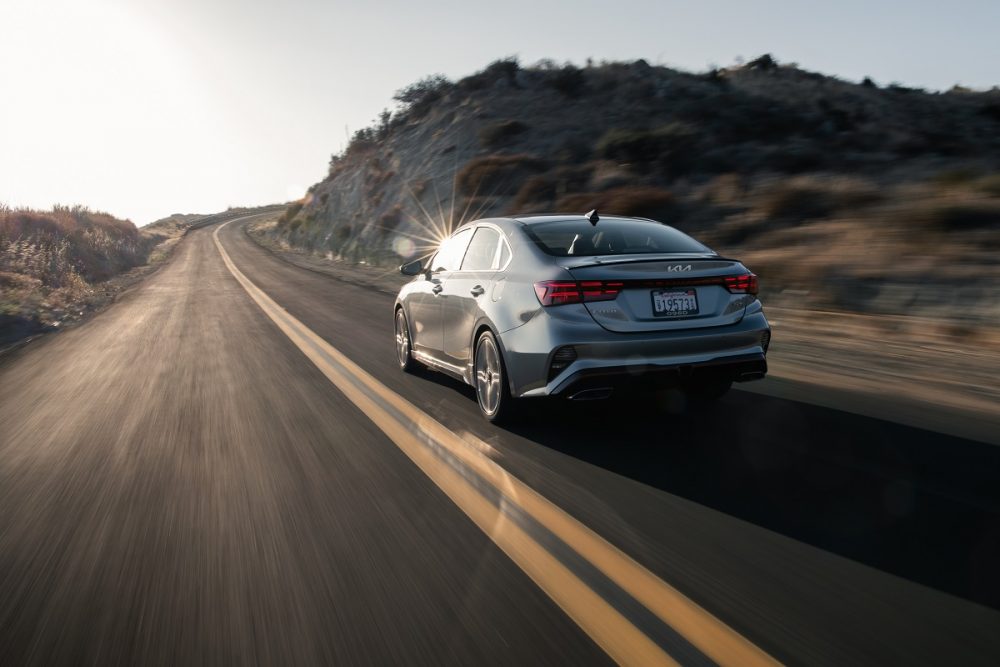 Rear view of a silver 2022 Kia Forte driving on a highway at sunset