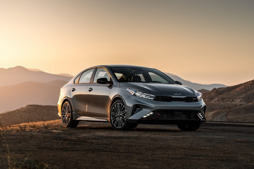 Front exterior view of a gray or silver 2022 Kia Forte parked on dirt at sunset