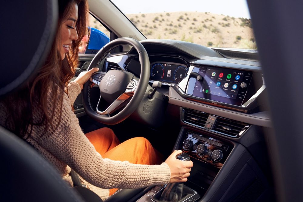 A woman sits behind the wheel of the 2022 Volkswagen Taos with her hand on the gear shifter