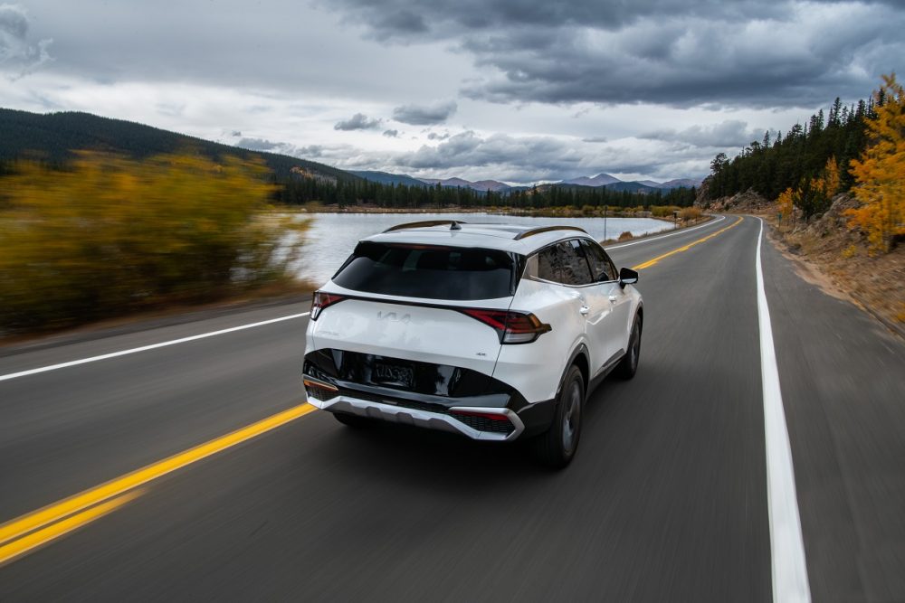 Rear view of a white 2023 Kia Sportage SX driving down a highway