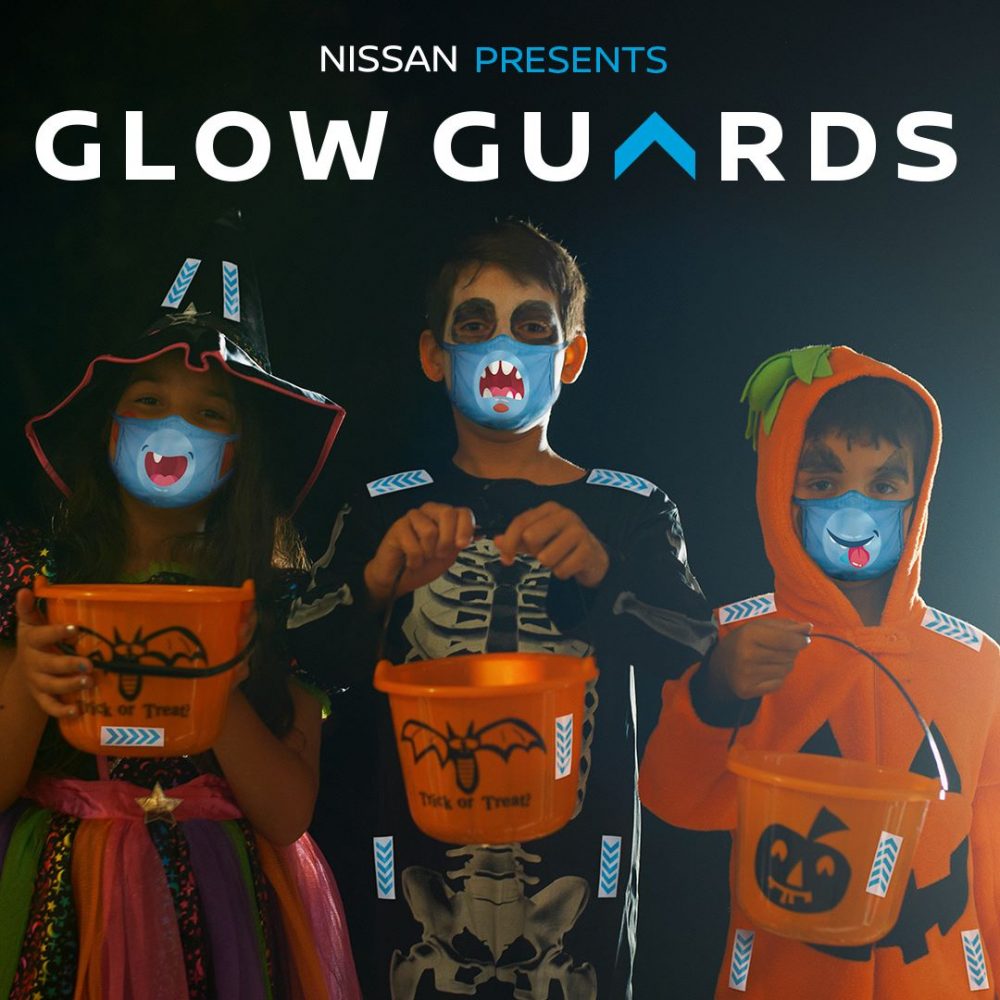 Three children dressed up for Halloween wear masks and Glow Guards, reflective stickers for trick or treating