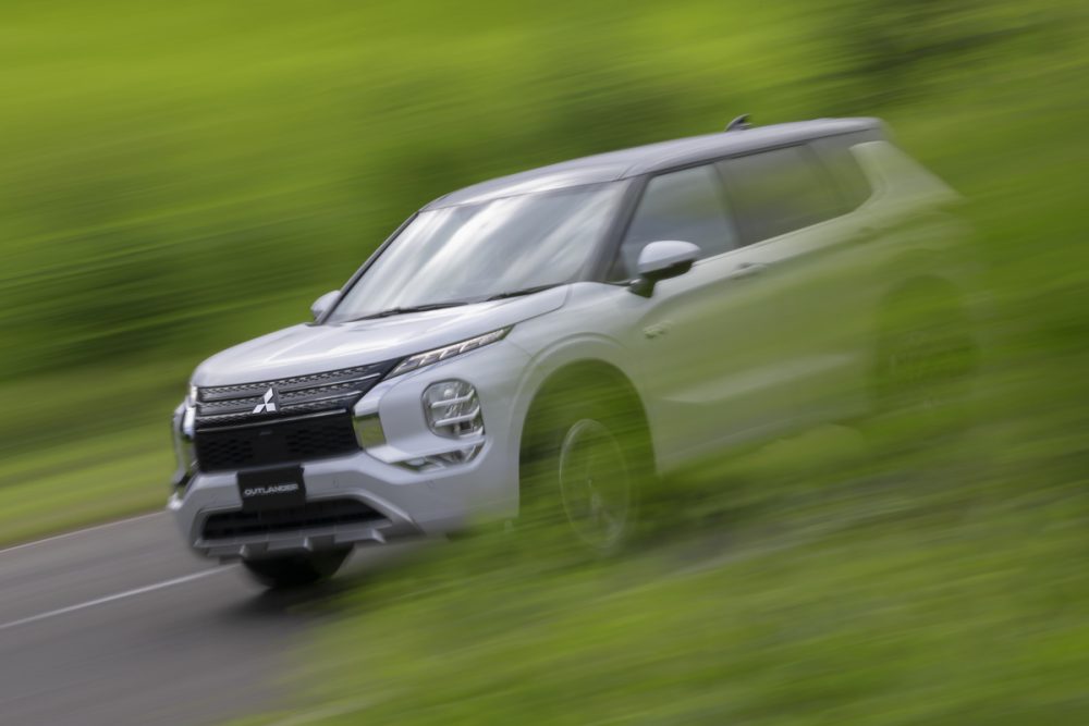 The 2023 Outlander PHEV driving past green trees