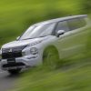 The 2023 Outlander PHEV driving past green trees