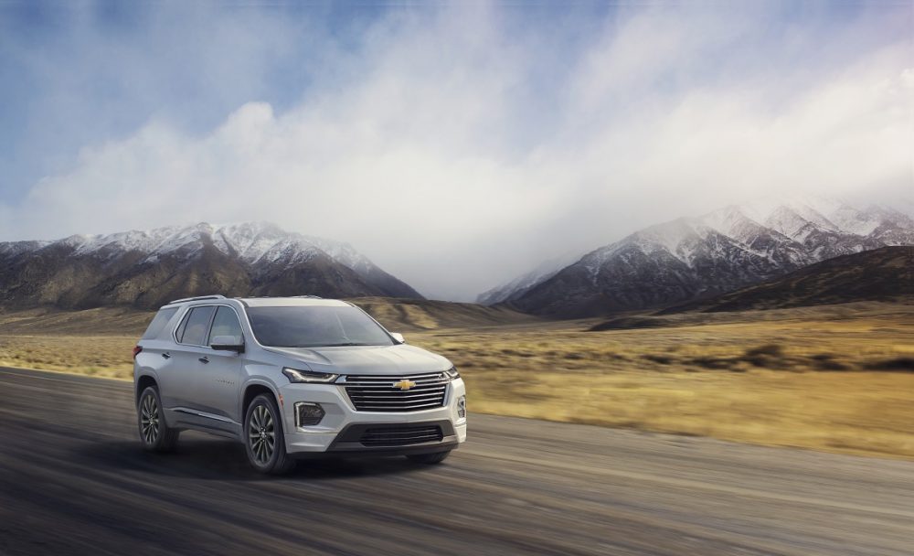 Front side view of 2022 Chevrolet Traverse Premier driving down road with clouds and mountains in background