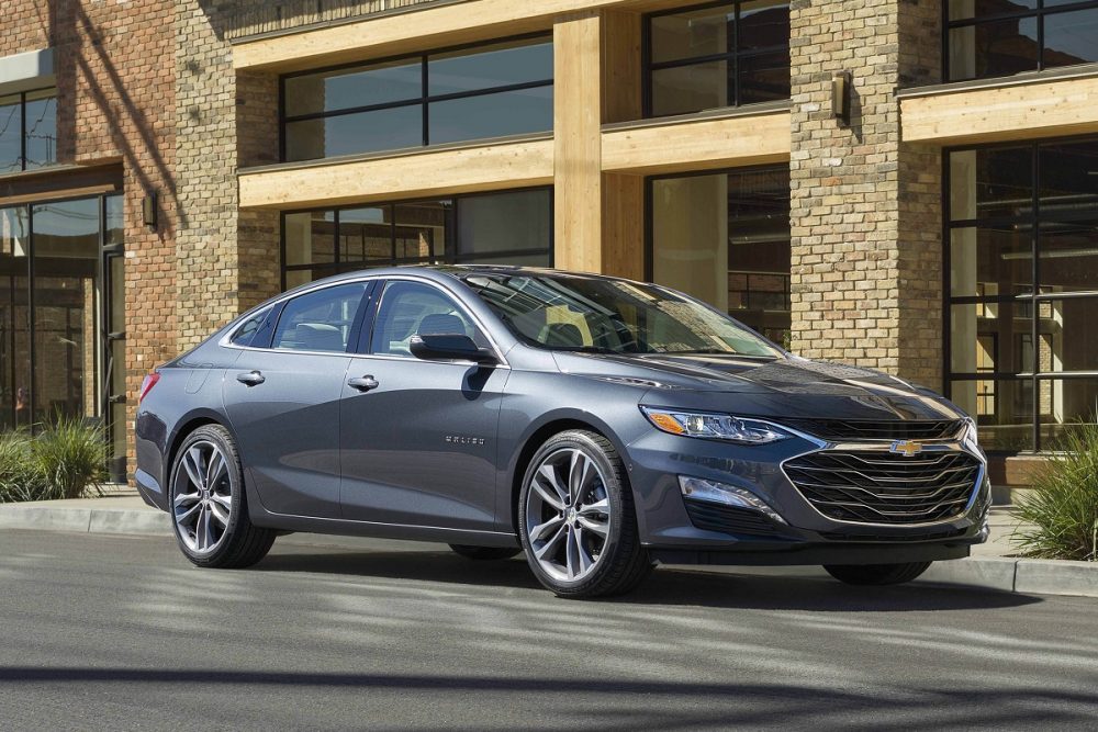 A gray 2022 Chevrolet Malibu parked in front of a city building