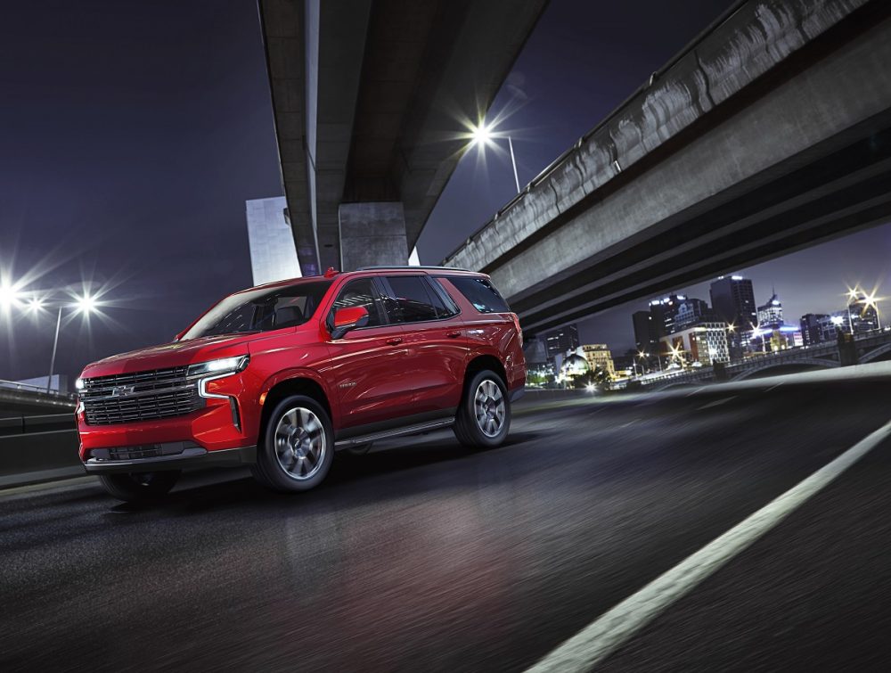 Front side view of red 2022 Chevrolet Tahoe RST driving down city street at night