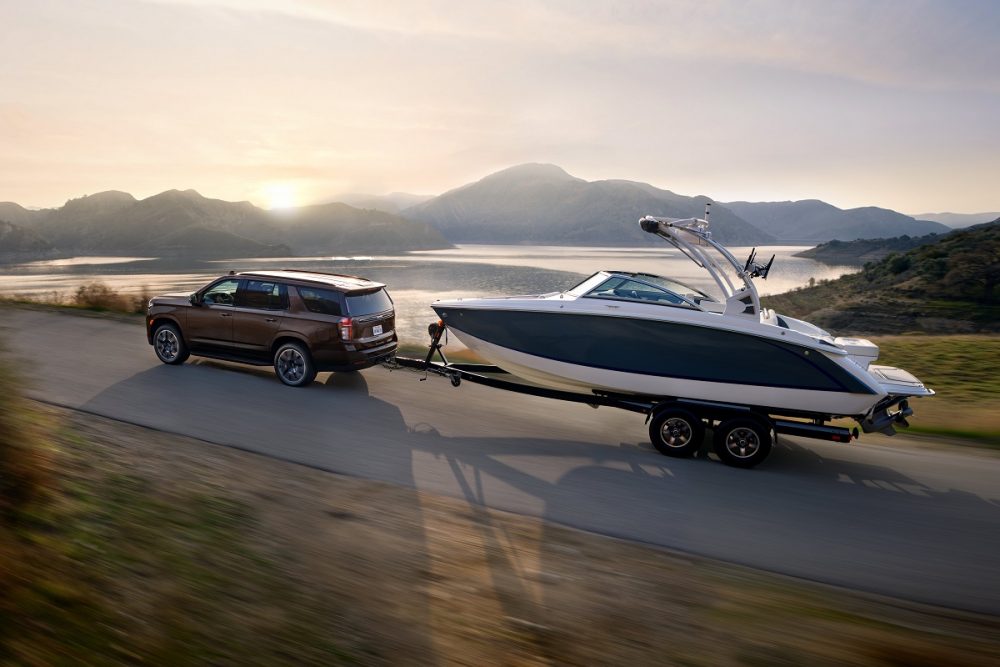 Rear side view of 2022 Chevrolet Tahoe RST pulling boat and trailer with water and mountains in background