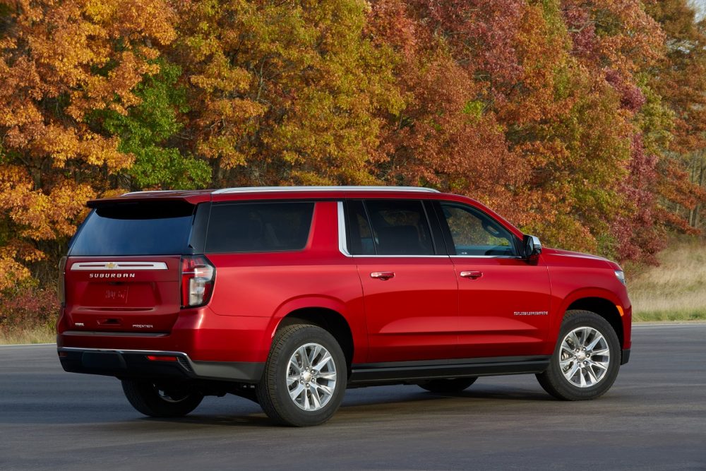 Rear side view of red 2022 Chevrolet Suburban Premier parked against backdrop of colorful fall leaves